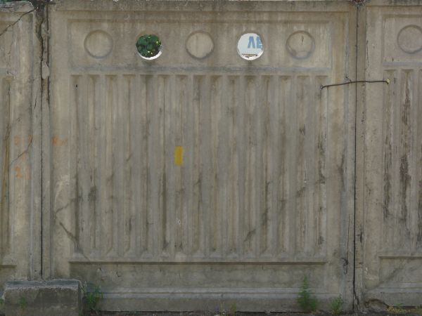 Concrete fence texture molded with a pattern of circles above vertical recessions, with large cracks and stains. The fence appears to be crumbling around the edges.